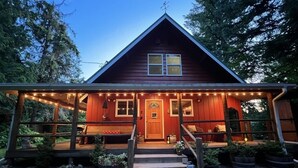 A wooden cabin with a porch, steps, and string lights. - Riverfront Cabin! BBQ, HOT TUB, FIRE PIT, 4 BEDROOMS (Baring)
