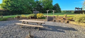 Un área de picnic con una mesa y bancos de madera, rodeada de grava y vegetación.