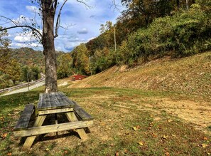 Une table de pique-nique dans un parc, avec un arbre à proximité et une route en arrière-plan.