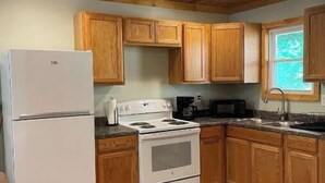 A kitchen with wooden cabinets, a white refrigerator, a stove, and a window. - Country Charm (Williamson)