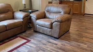 A cozy living room with two leather armchairs, a small table, and a red rug. The room features wooden flooring and a wooden ceiling with recessed lighting. - Country Charm (Williamson)