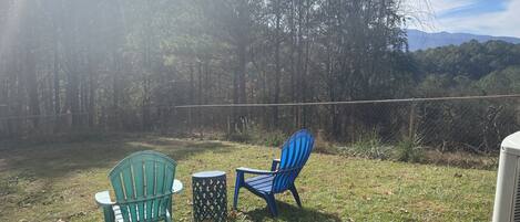 An outdoor seating area with two chairs and a small table, surrounded by a chain-link fence and trees.