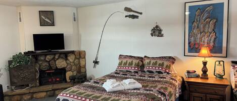 Una habitación acogedora con chimenea, una cama con cubrecama con motivos forestales, un televisor y un cuadro de peces en la pared.