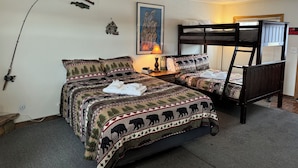 A room with two beds, a bunk bed, a fishing rod, a welcome sign, a painting, and a 'No Smoking' sign. - The fishing suite (Red Feather Lakes)