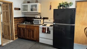A compact kitchen with wooden cabinets, a microwave, a stove, and a black refrigerator. - The fishing suite (Red Feather Lakes)