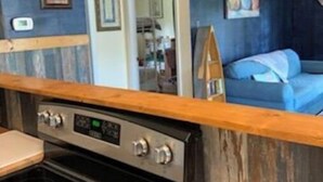 Une cuisine compacte équipée d’une cuisinière et d’un four, d’un plan de travail en bois et d’un mur bleu orné d’un tableau.
