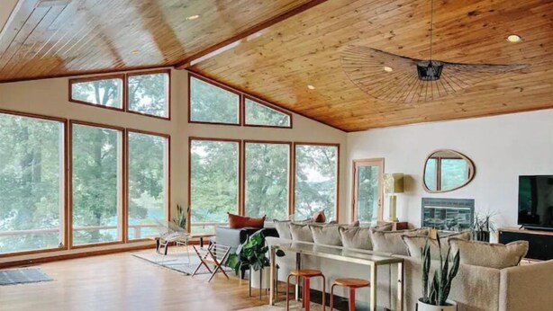 Un salon spacieux avec de grandes fenêtres, un plafond en bois et un canapé moderne.
