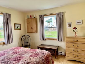 A bedroom with a bed, a wooden dresser, a chair, a wooden bench, and a window with curtains.