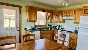 A kitchen with wooden cabinets, a dining table, chairs, a refrigerator, a stove, a microwave, and a dishwasher. - Montgomery Cavendish Cottages (Cavendish)