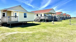 A row of small, single-story cabins with porches, numbered 68, set in a grassy area under a clear sky. - Montgomery Cavendish Cottages (Cavendish)