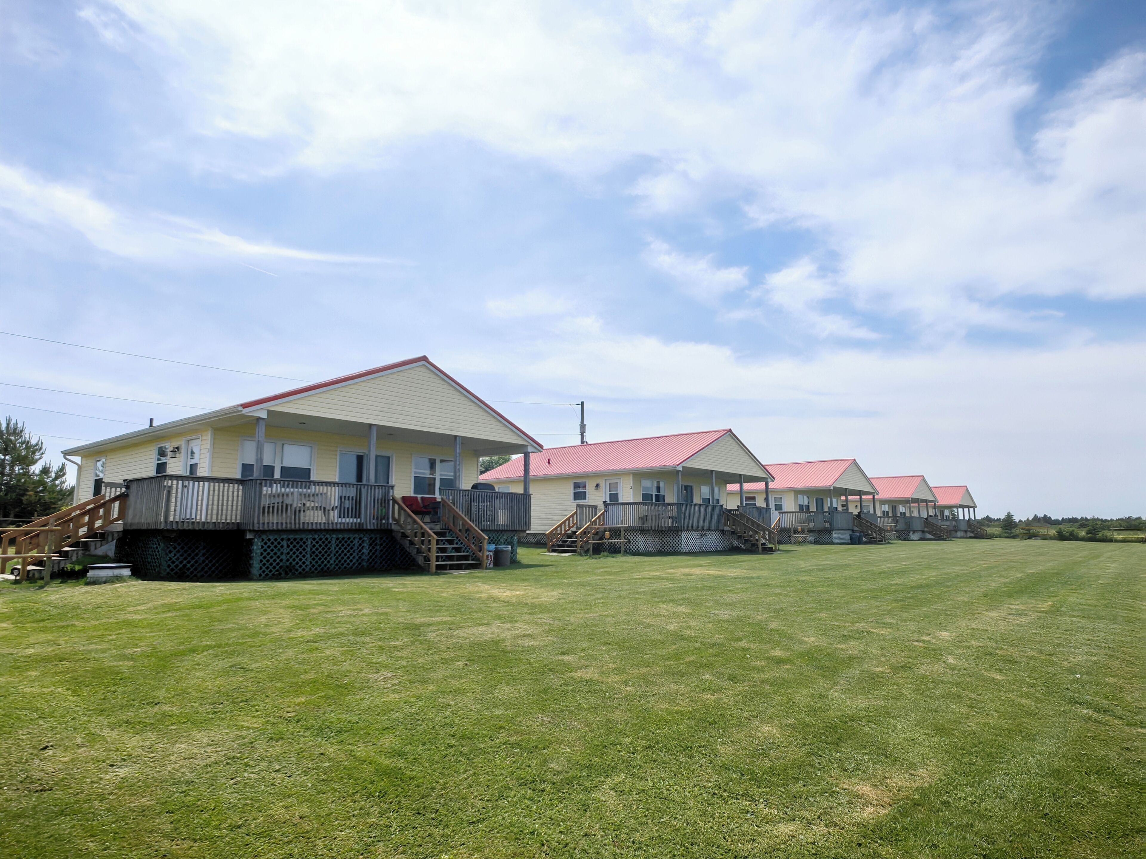 A row of single-story cabins with attached porches and a grassy field in the foreground.