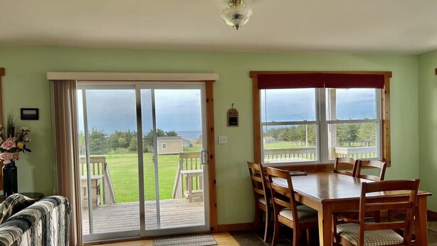 A dining area with a wooden table and chairs, a sliding glass door leading to a deck, and a view of the outdoors. - Montgomery Cavendish Cottages (Cavendish)
