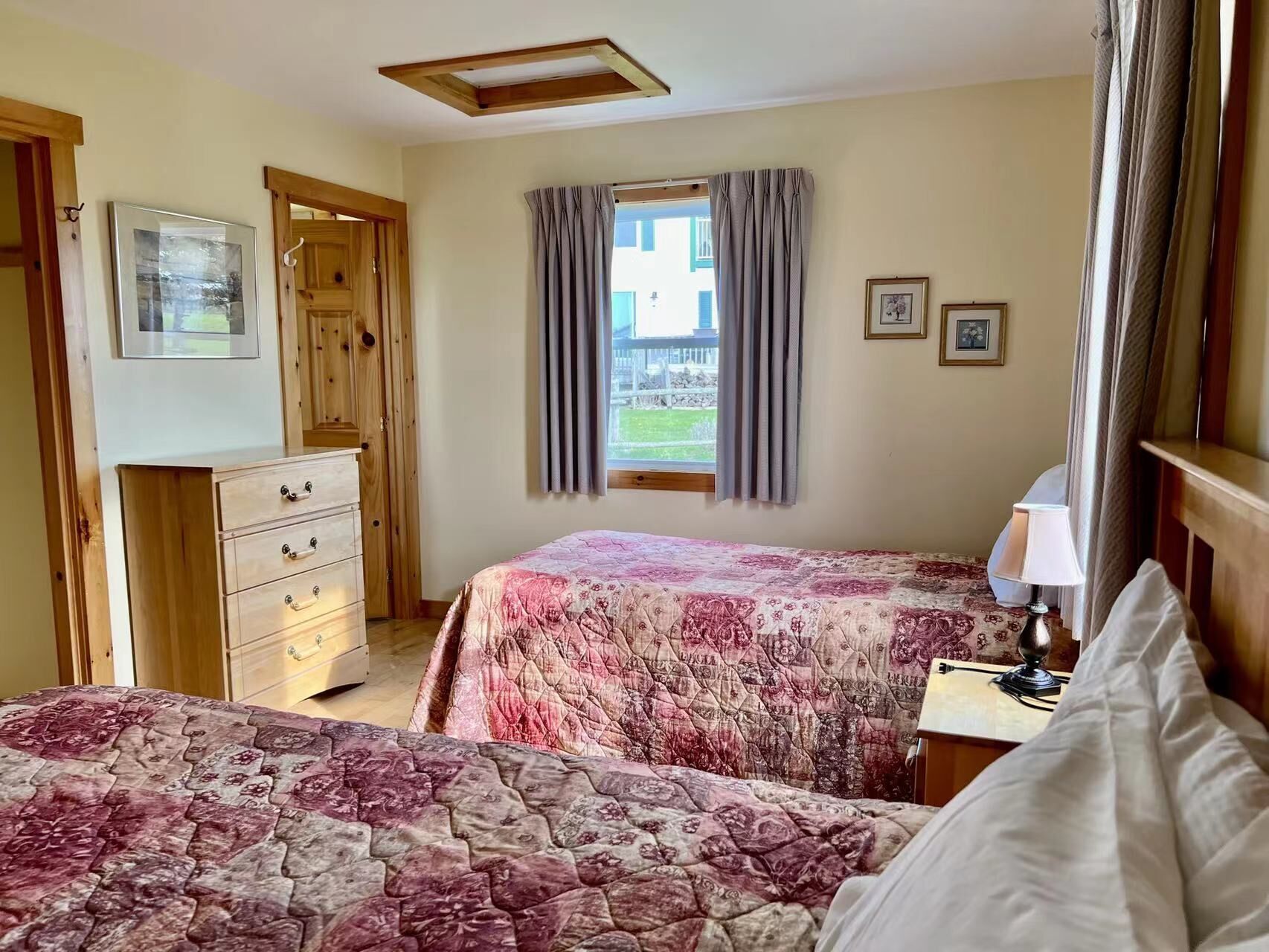 A bedroom with two beds, a dresser, a lamp, and a window with curtains.