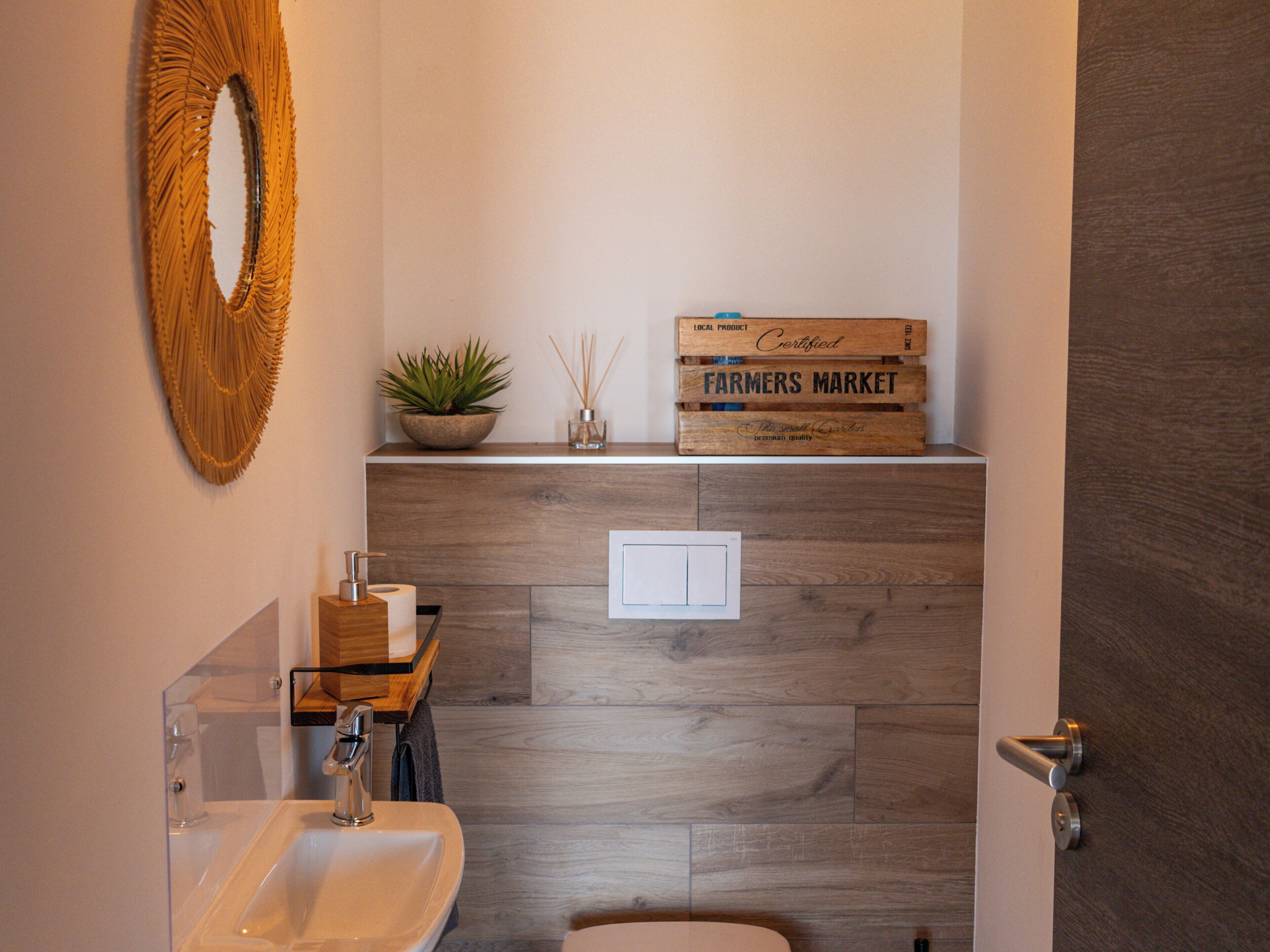Een moderne badkamer met een houten wastafelmeubel, een wastafel, een spiegel en een decoratieve plant.