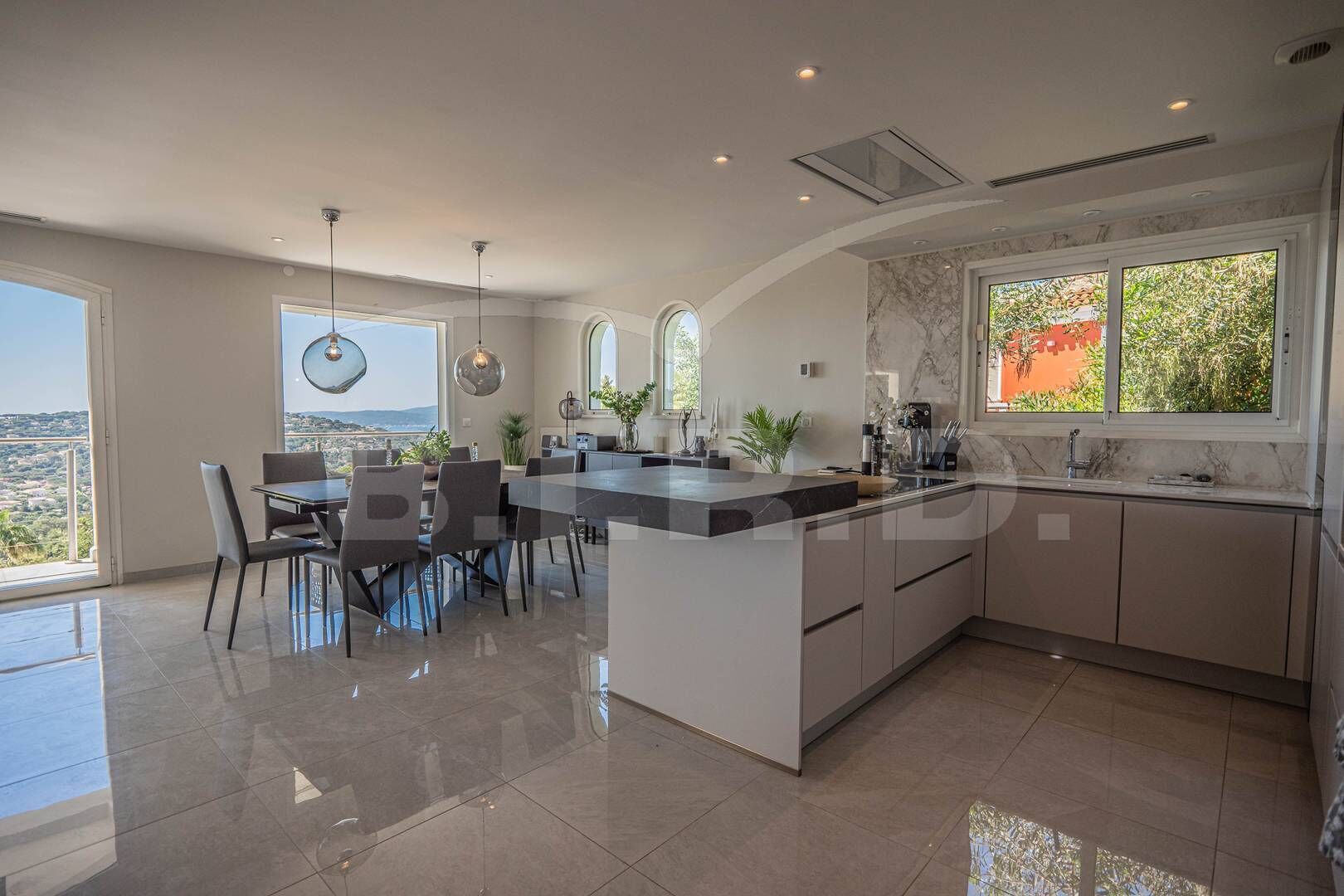A modern kitchen with a large island, dining area, and large windows offering a view.