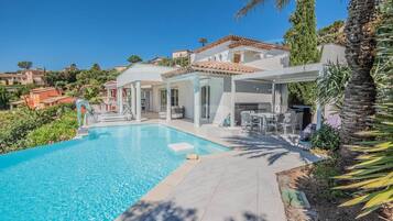 A poolside area with a clear blue pool, outdoor seating, and a covered patio.