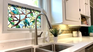 A kitchen with a stainless steel sink, a window with a stained glass design, and white cabinets.
