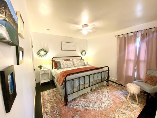 Un dormitorio con cama, mesita de noche, silla y coronas decorativas.