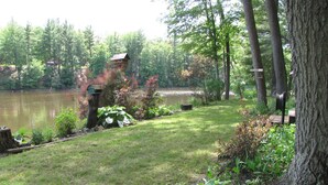 A serene lakeside garden with a wooden birdhouse, a pond, and lush greenery. - Nature lovers retreat right on the edge of the river (Hersey)