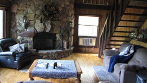 A cozy living room with a stone fireplace, wooden beams, and a staircase. - Nature lovers retreat right on the edge of the river (Hersey)