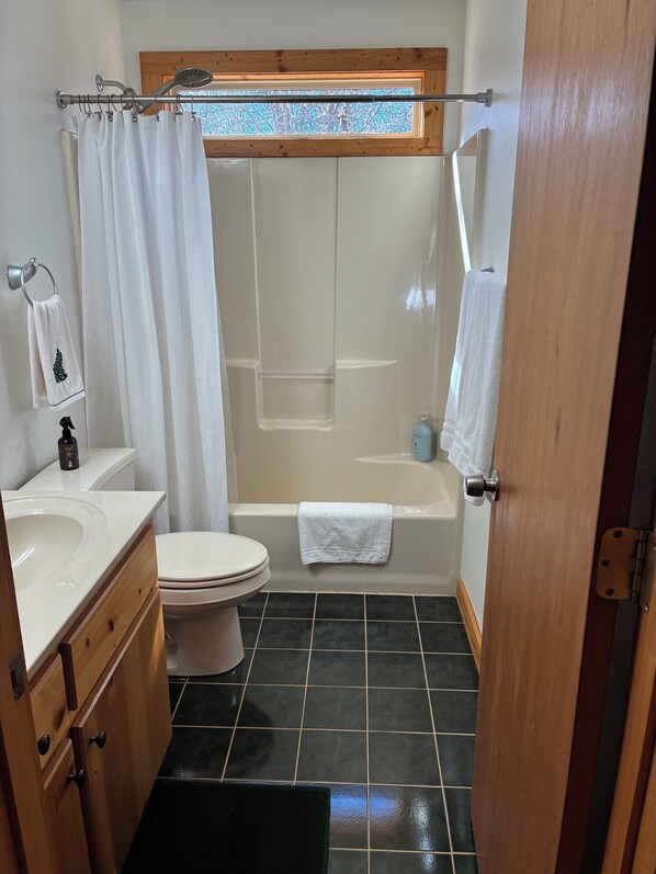 A bathroom with a toilet, sink, bathtub, and shower curtain. - Almost Perfect Cabin (Lavonia)