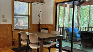 Un comedor de madera con una mesa, sillas, un perchero y vistas a muebles de exterior a través de un ventanal.