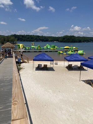 A beach with a wooden walkway, blue canopies, and inflatable water play structures. - Almost Perfect Cabin (Lavonia)