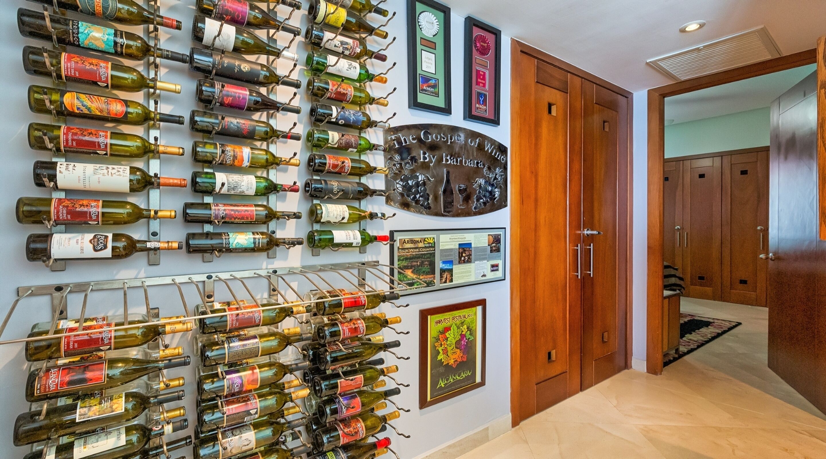 A wine cellar with numerous bottles and wine racks, a wooden door, and framed awards on the wall.