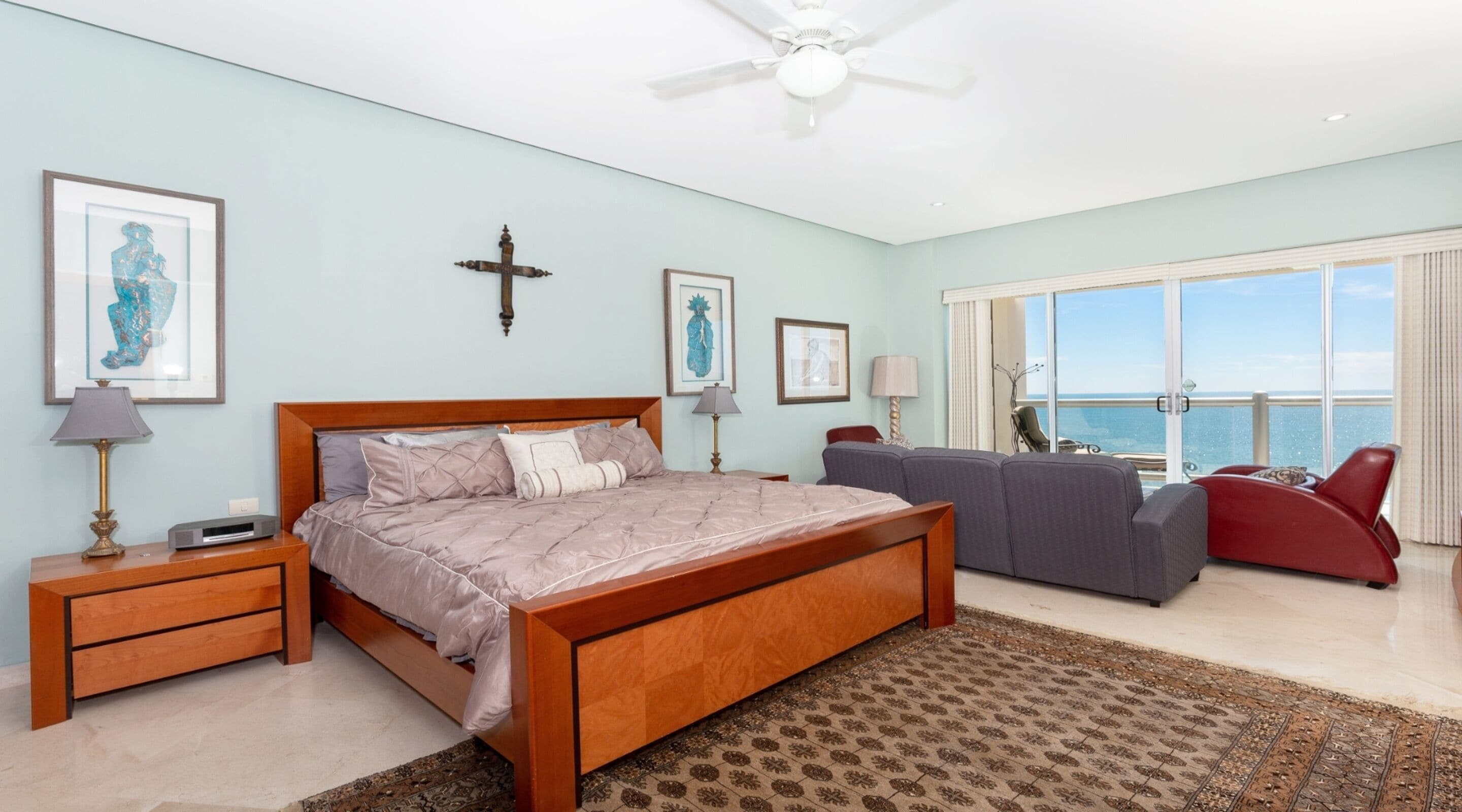 A bedroom with a large bed, a sofa, a red chair, and a view of the sea through a large window.