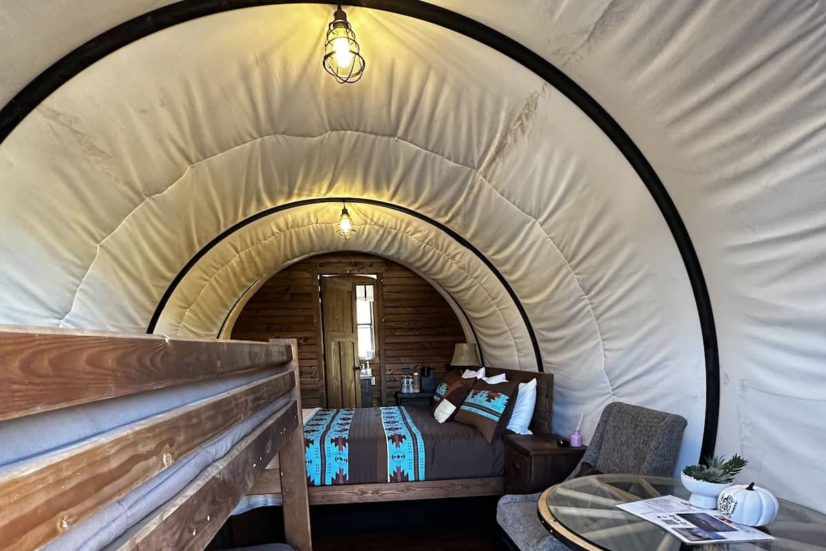 A cozy interior of a tent-like accommodation with a bed, seating area, and a small table.