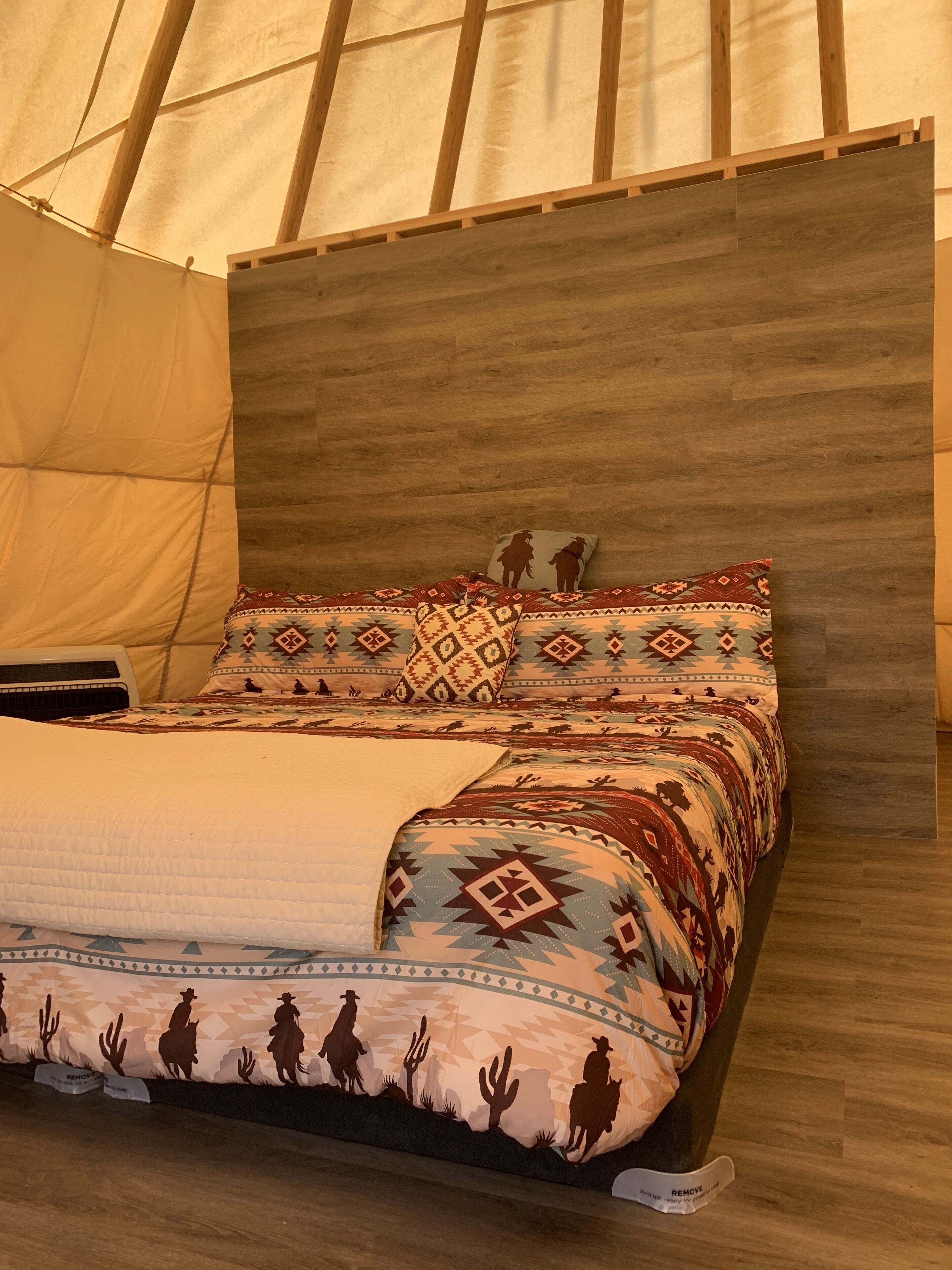 A bed with patterned bedding and a wooden headboard in a tent-like structure.