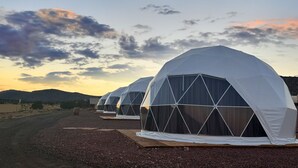 A row of geodesic dome tents with a gravel ground and a mountainous backdrop. - Grand Canyon Glamping Resort (Meadview)