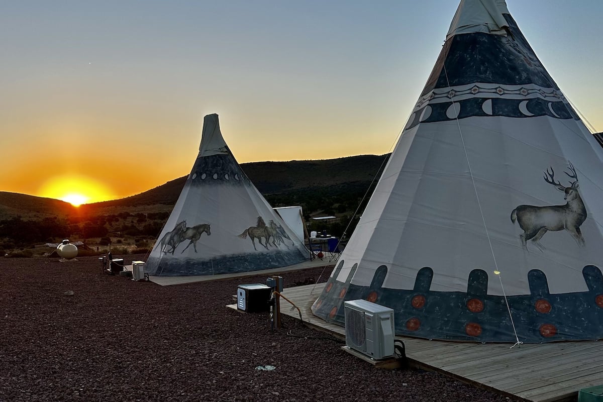 Two large conical tents with wildlife designs, set on a gravel surface with a sunset in the background.