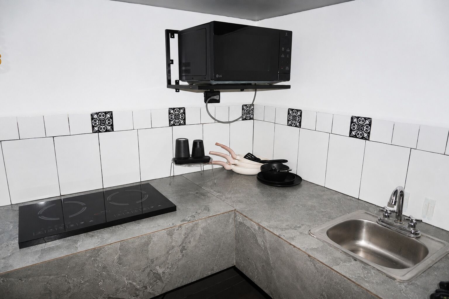 A kitchen with a black microwave, a stove, a sink, and a chair.