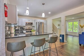 A modern kitchen with stainless steel appliances, a bar area with stools, and a view of the outdoors through large windows.
