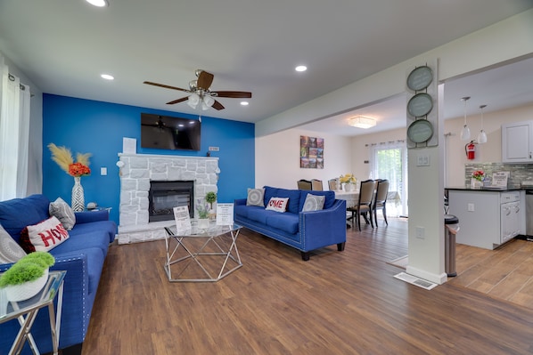 A modern living room with a blue accent wall, a stone fireplace, and a ceiling fan.
