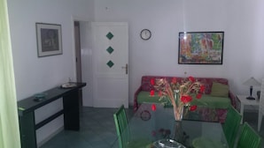 Un comedor con una mesa de vidrio, sillas, un sofá, un reloj y una puerta con adornos en forma de rombos.