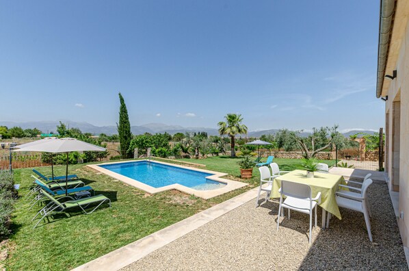 Ein Garten mit Swimmingpool, Rasenfläche, weißen Stühlen und Sonnenschirmen.