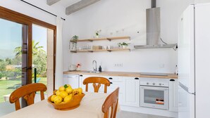 A modern kitchen with white cabinets, wooden countertops, and a built-in oven. There is a dining table with chairs and a bowl of lemons.