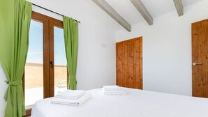 A bedroom with a bed, green curtains, wooden doors, and a view through a glass door.