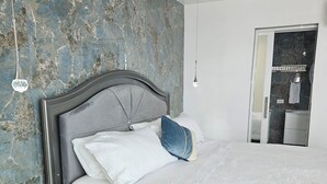 Ein modernes Schlafzimmer mit Marmorwand, einem Bett mit weißer Bettwäsche, einem dunklen Nachttisch mit Schubladen und einem Spiegel an der Wand.