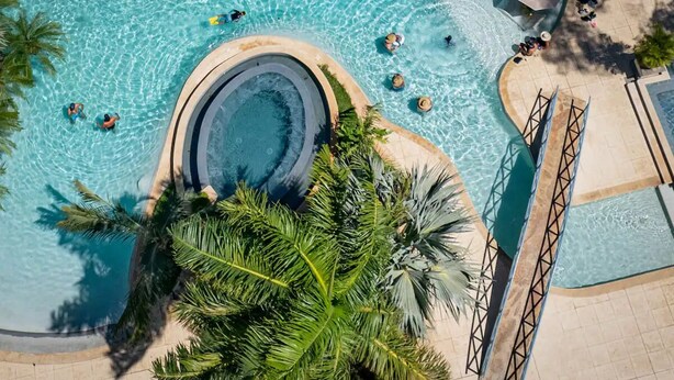 An aerial view of a swimming pool with clear water, surrounded by palm trees and a circular hot tub. - Ocean-View Condo / Lagoon Pool & Swim-Up Bar (Tamarindo)