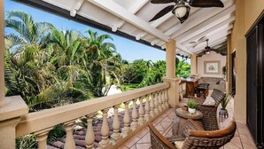 A covered outdoor area with a balcony, wicker furniture, ceiling fans, and lush tropical plants. - Ocean-View Condo / Lagoon Pool & Swim-Up Bar (Tamarindo)