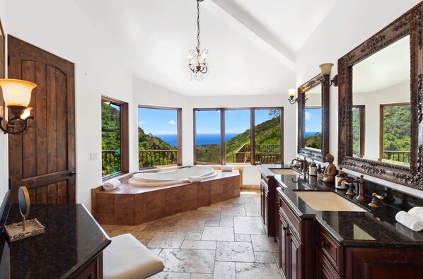 A luxurious bathroom with a large bathtub, a vanity with a mirror, and a view of the ocean.
