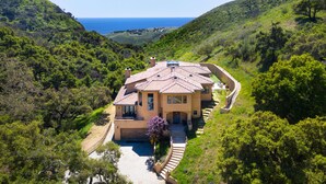 Ein Haus im mediterranen Stil mit Terrakotta-Dach, umgeben von üppiger Vegetation und Blick auf die Küste.