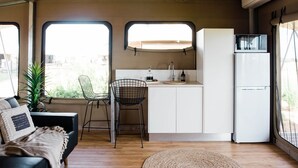 Una cocina compacta con un lavamanos, dos sillas, un refrigerador y un ventanal.