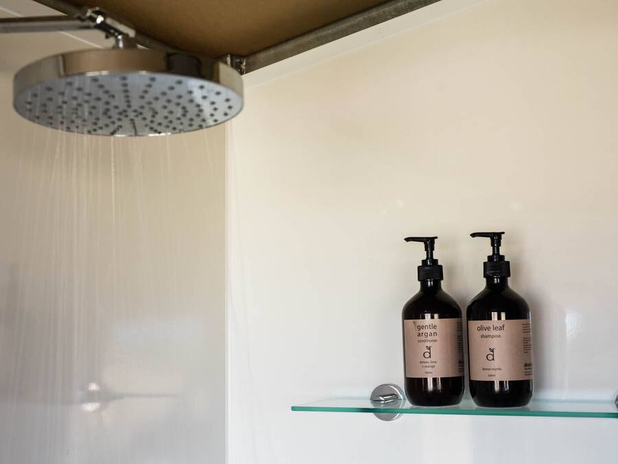 Une douche équipée d’un pommeau de douche à effet pluie et de deux bouteilles de shampoing posées sur une étagère en verre.
