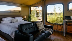 Un dormitorio con una cama, un sofá de cuero negro, una mesita y vistas a un jardín a través de amplios ventanales.
