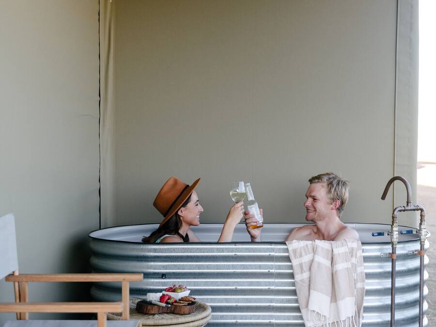 A hot tub with two people, a wicker chair, and a small table with a basket.