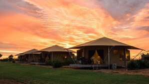 Una hilera de carpas con entradas abiertas, cada una con una mesa y sillas, frente a un cielo al atardecer.